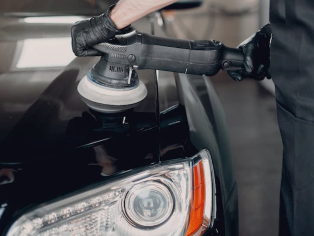 Profissional utilizando politriz no capô de um carro preto