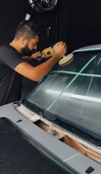Profissional polindo o para-brisa de um carro com politriz e fita crepe demarcando a área